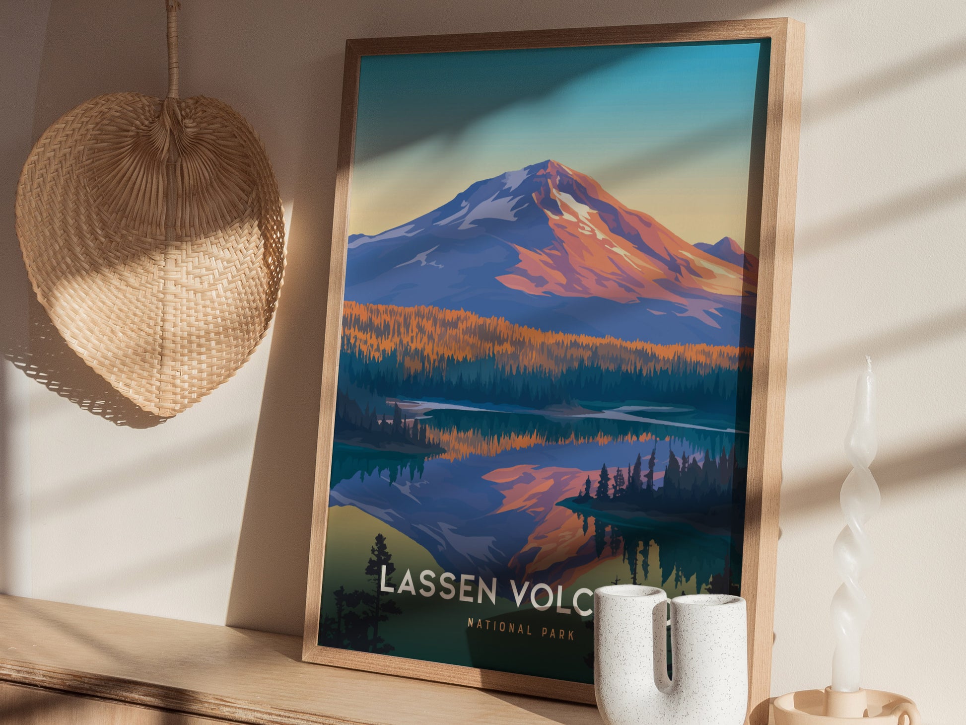 A framed poster of Lassen Volcanic National Park rests on a wooden shelf next to a woven basket and a white decorative candle. Sunlight casts soft shadows across the scene.