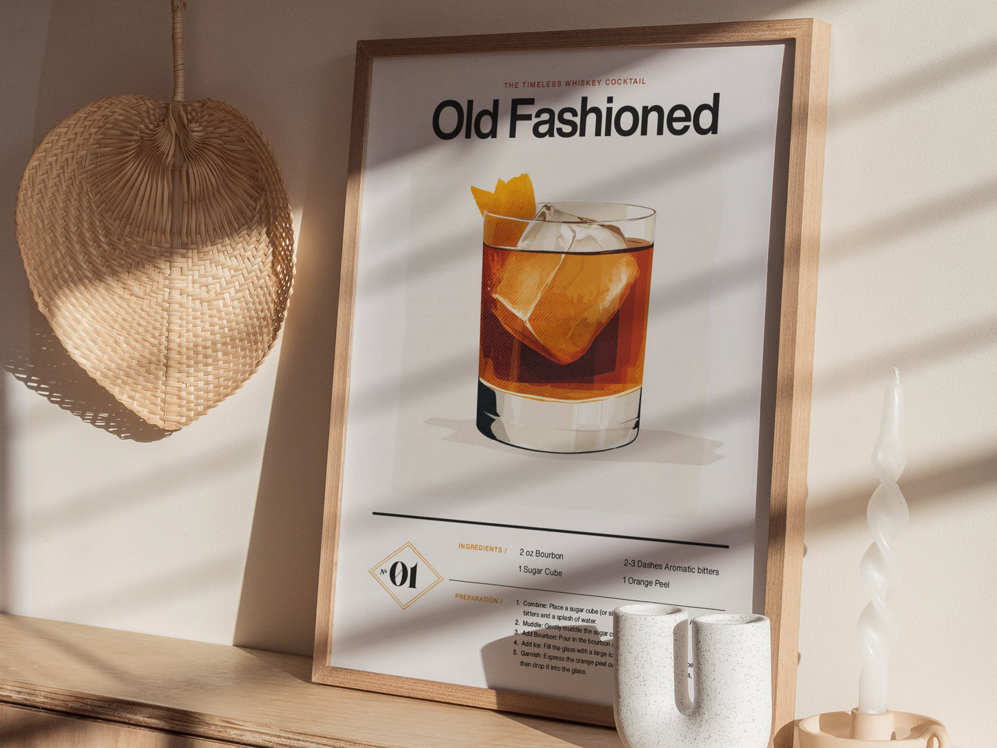 A framed Old Fashioned cocktail poster with a whiskey glass illustration is displayed on a wooden shelf, accompanied by a woven fan and a twisted white candle.