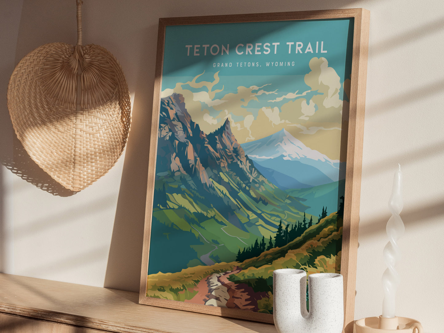 A framed poster of the Teton Crest Trail is displayed on a wooden shelf, accompanied by a textured wall hanging and a modern candle holder. Natural light casts soft shadows.