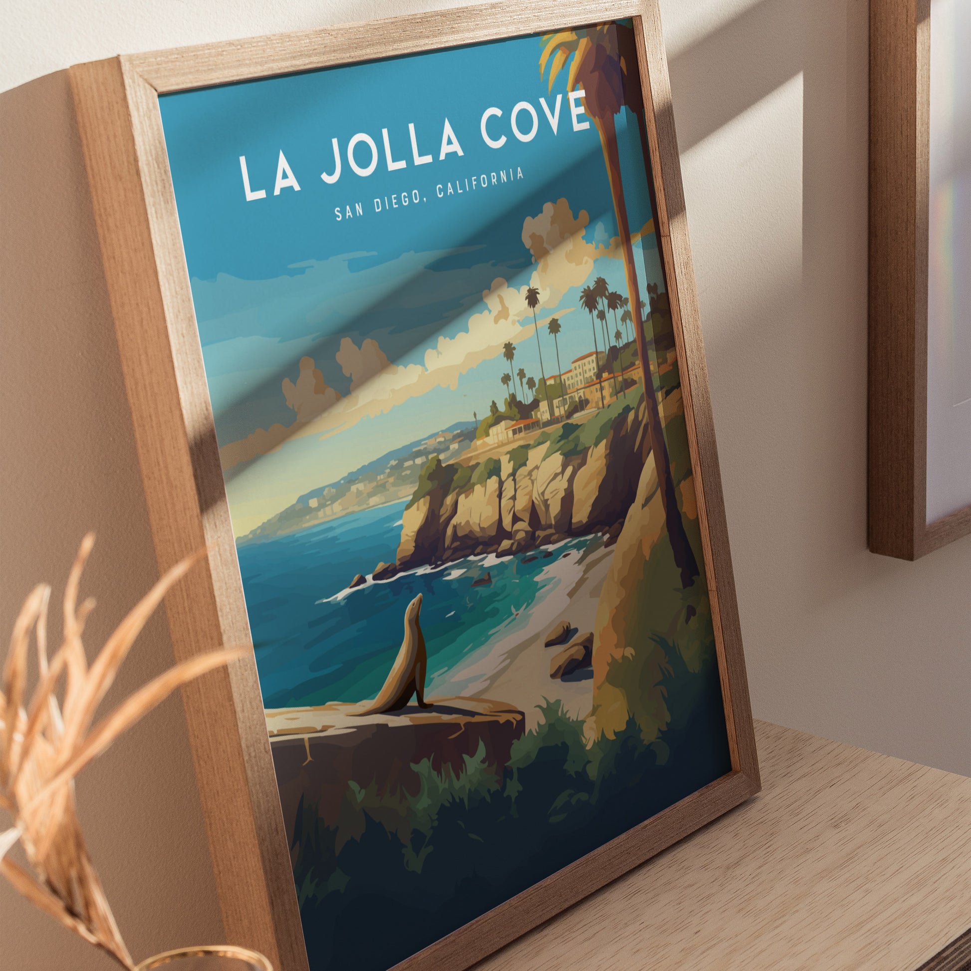 Framed poster of La Jolla Cove features a scenic coastline with sea cliffs, palm trees, and a seal on a rock, set against a vibrant blue sky.