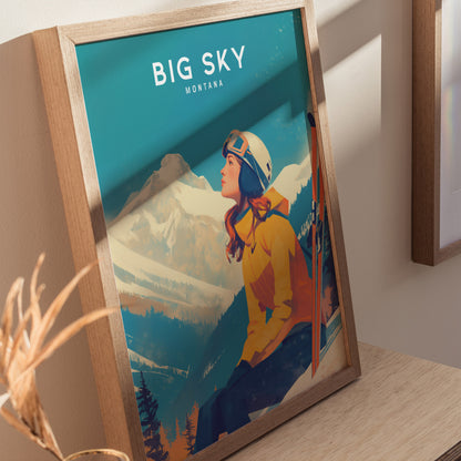 A framed poster titled Big Sky Montana features a woman in a yellow jacket and helmet, gazing at snow-covered mountains. The artwork is displayed on a wooden surface.