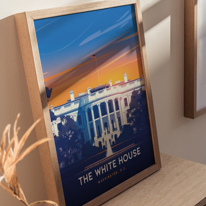 Framed poster of the White House with a vibrant sunset background, featuring bold colors and clean lines. The artwork is displayed on a wooden surface, creating a warm ambiance.