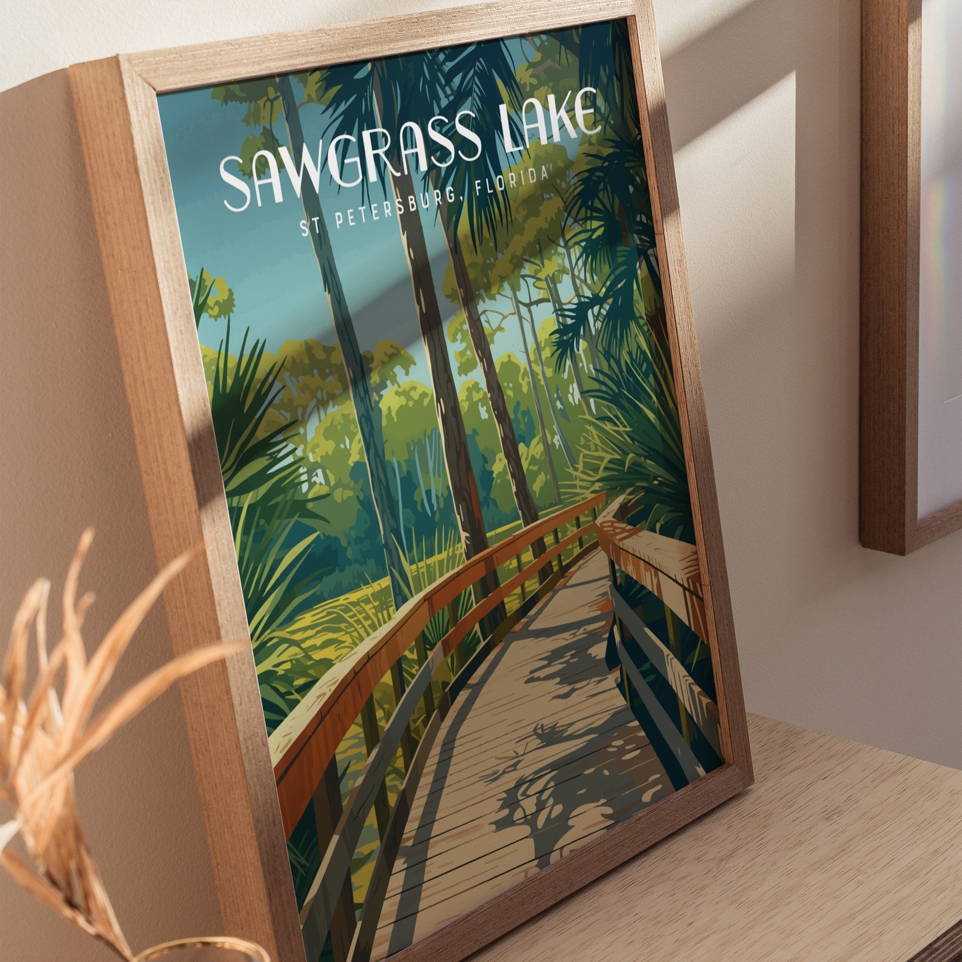 Framed poster of Sawgrass Lake Park in St. Petersburg, Florida, showcasing a wooden boardwalk through lush greenery and trees. The artwork is vibrant and detailed, resting on a wooden surface.