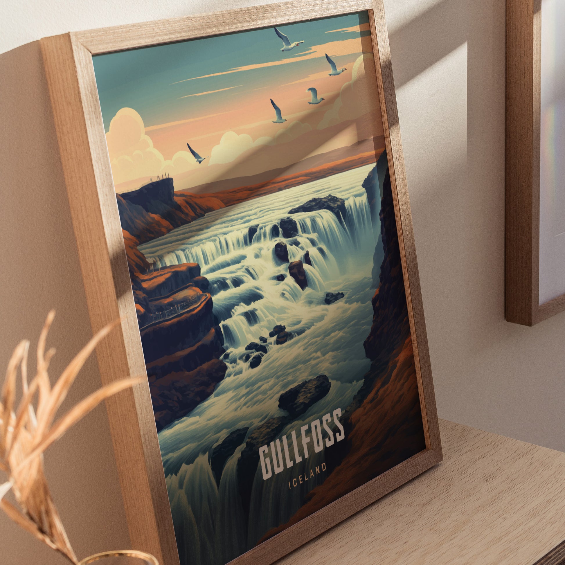 A framed poster depicting Gullfoss waterfall in Iceland, with cascading water under a pastel sky and flying birds, displayed on a wooden surface.