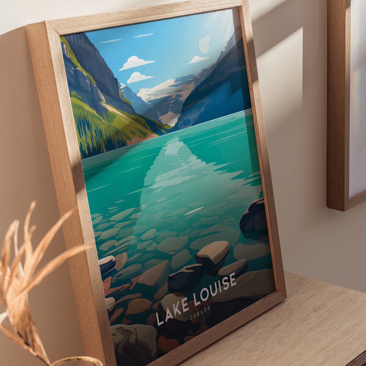 Framed Lake Louise poster depicting turquoise water and mountain landscape, with Lake Louise Canada text at the bottom. The artwork is displayed on a wooden surface with natural lighting.