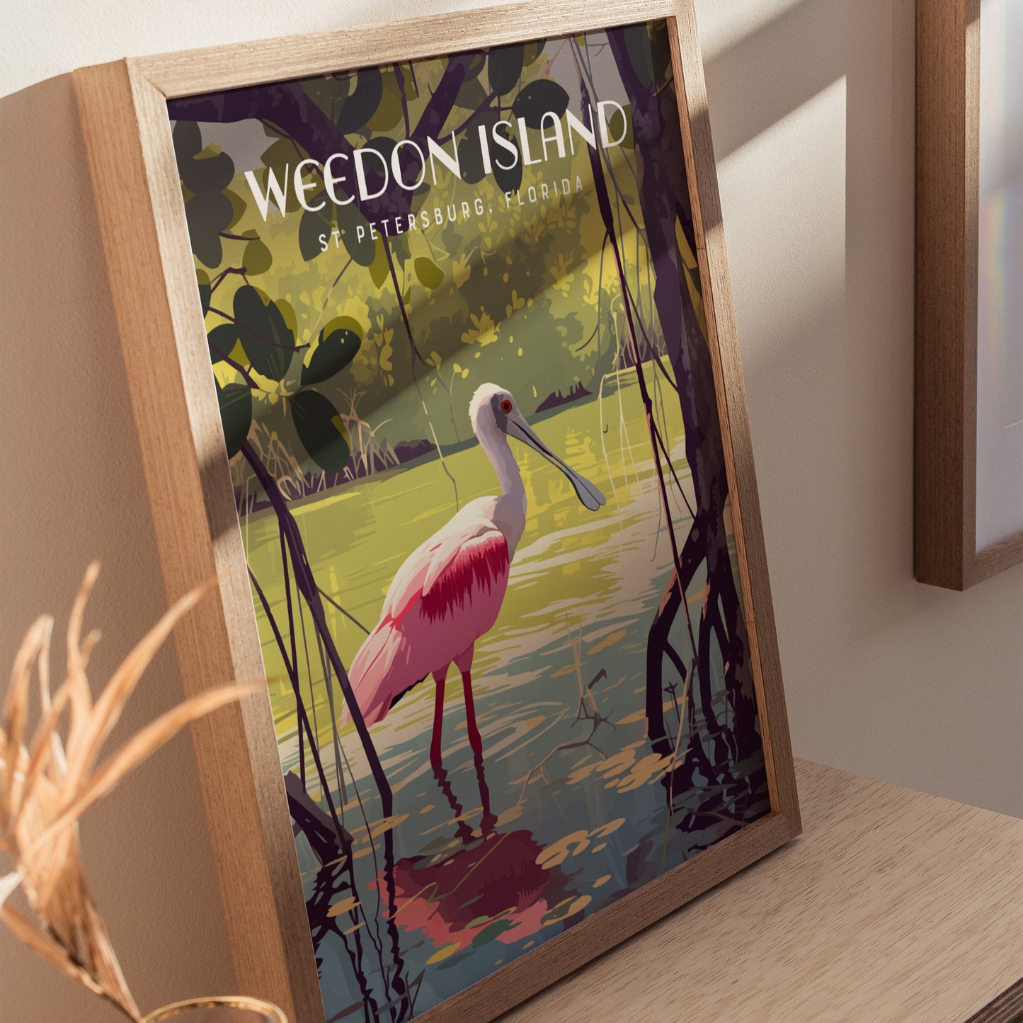 Framed artwork of a pink Roseate Spoonbill wading in mangrove waters, with Weedon Island, St. Petersburg, Florida text. The vibrant image highlights serene natural beauty in a wooden frame.