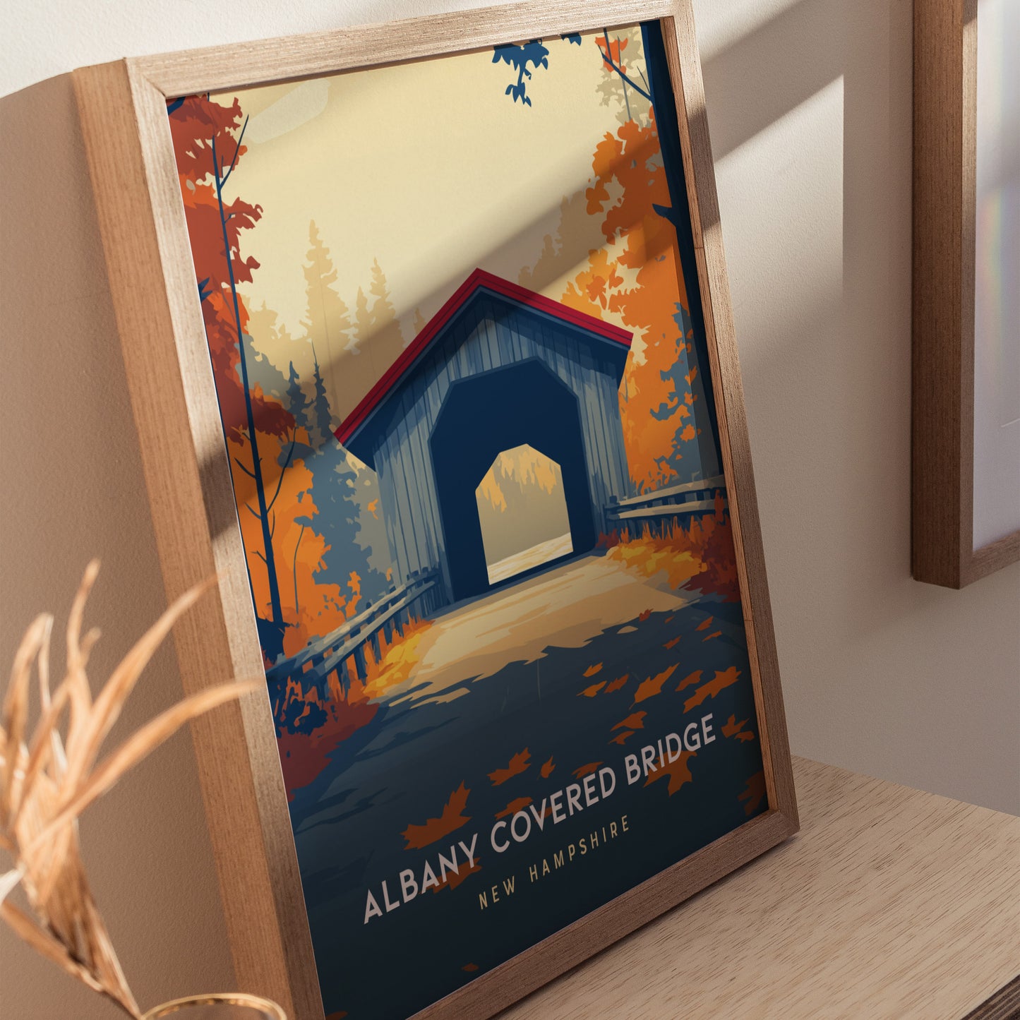 A framed poster of the Albany Covered Bridge in New Hampshire, showcasing a vibrant autumn scene with rich orange and red foliage. The bridge is depicted against a serene backdrop, highlighting the beauty of the landscape.