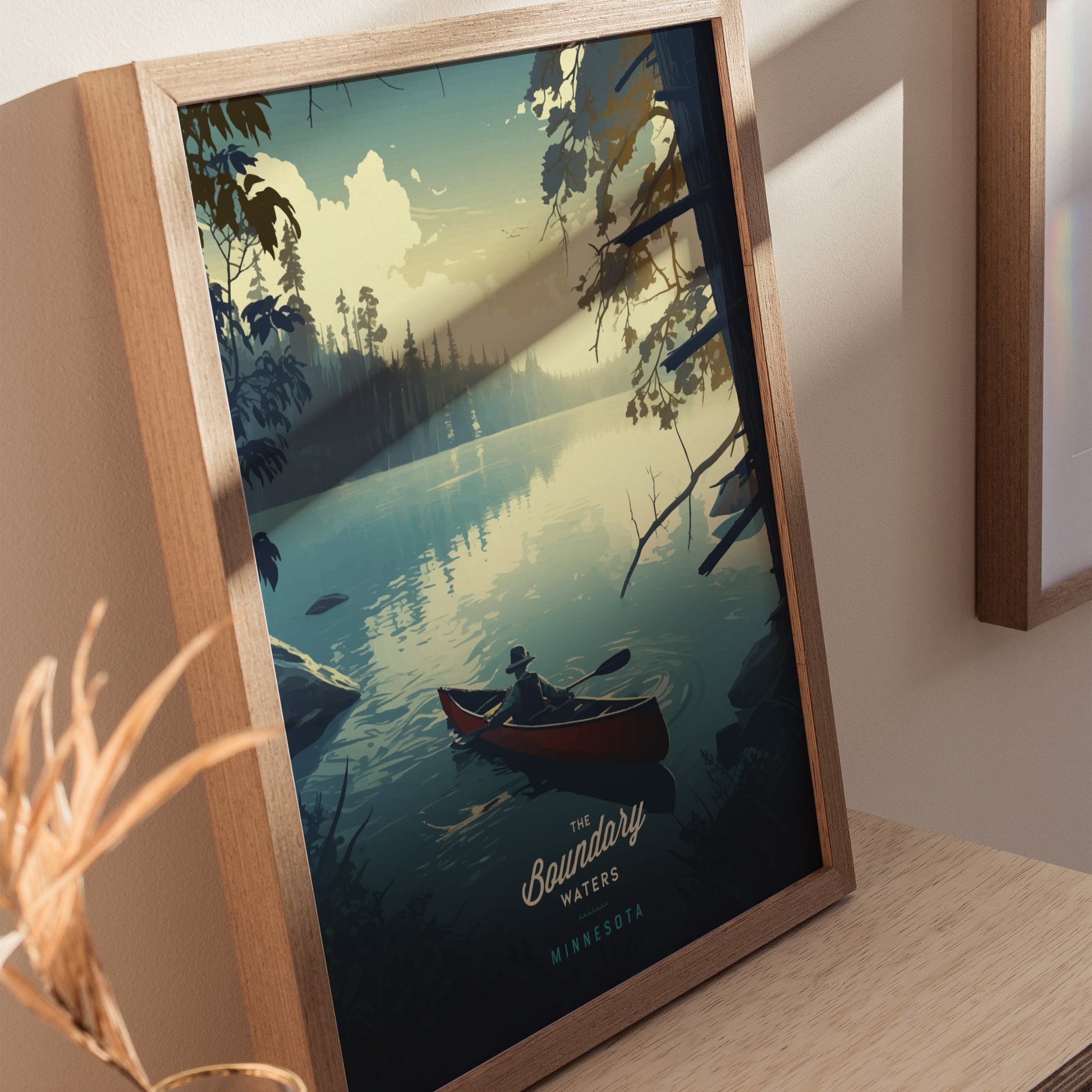 Framed artwork depicting a serene scene of a person paddling a canoe on a tranquil lake, surrounded by forest and a dramatic sky, titled The Boundary Waters Minnesota.