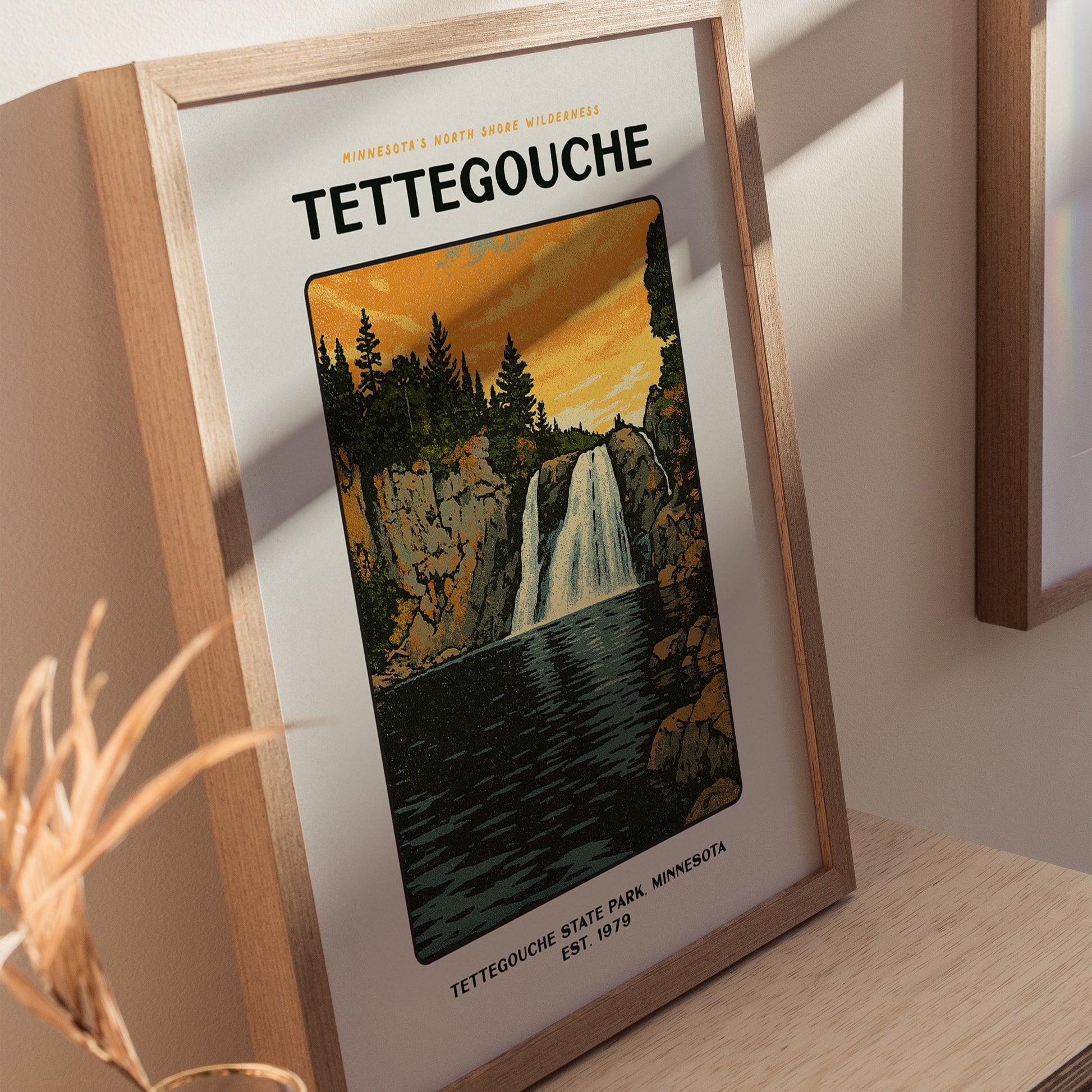 Framed poster of Tettegouche State Park featuring a waterfall cascading through cliffs, surrounded by trees, under a vibrant orange sky. The text highlights Minnesotas North Shore wilderness.