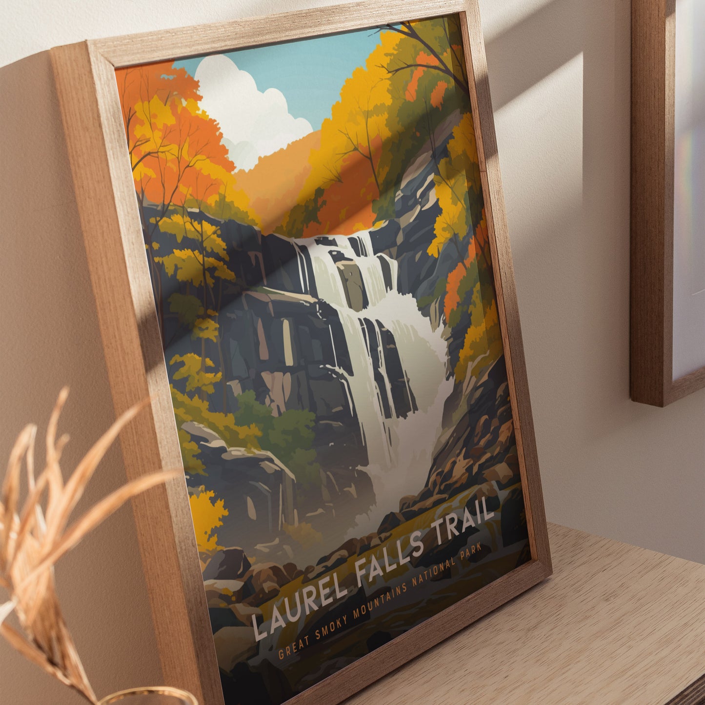 Framed poster of Laurel Falls Trail depicting a waterfall surrounded by vibrant autumn foliage, displayed on a wooden surface with soft natural lighting.