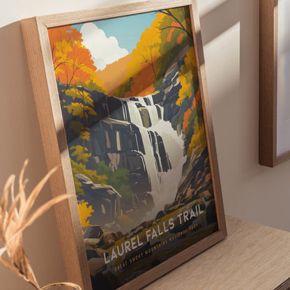 Framed poster of Laurel Falls Trail depicting a waterfall surrounded by vibrant autumn foliage, displayed on a wooden surface with soft natural lighting.