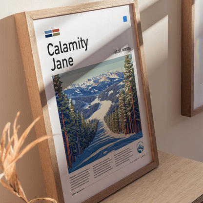 Framed poster titled Calamity Jane featuring a ski run through snow-covered pines at Big Sky, Montana. Sunlight casts shadows on the wooden frame and surrounding wall.