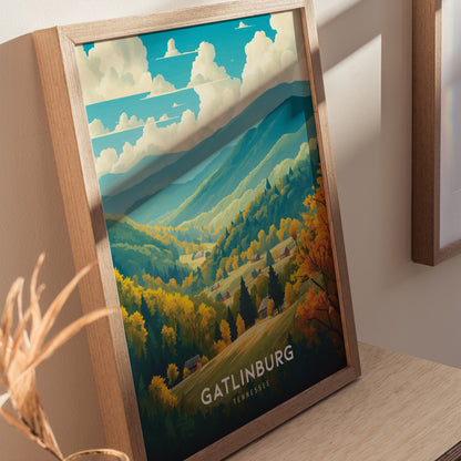 A framed Gatlinburg poster rests on a wooden surface, depicting a vibrant landscape of Tennessee mountains with lush forests and rolling hills under a partly cloudy sky.