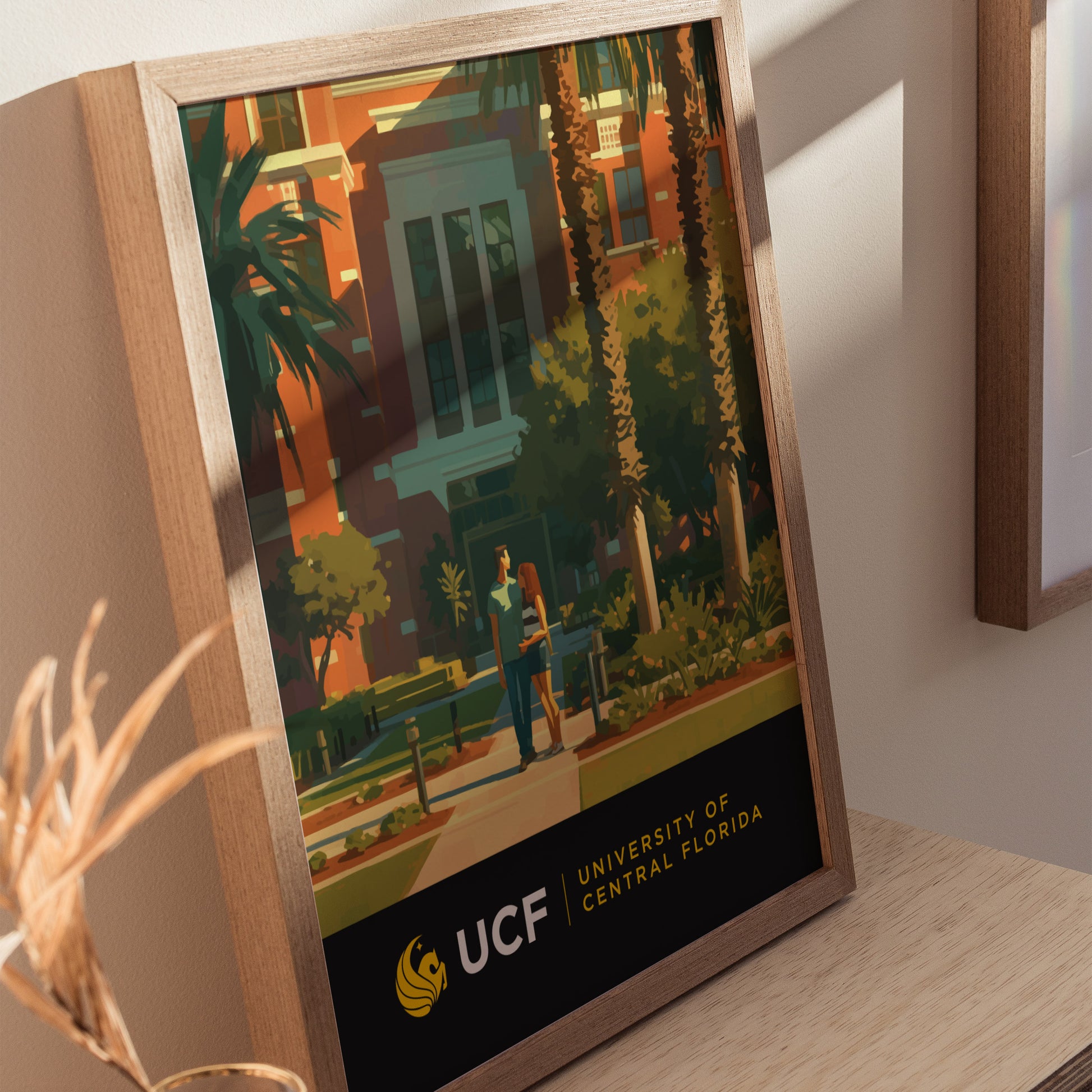 Framed poster featuring a vibrant illustration of the University of Central Florida campus, showcasing palm trees, modern architecture, and two people walking. UCF logo and name displayed below.