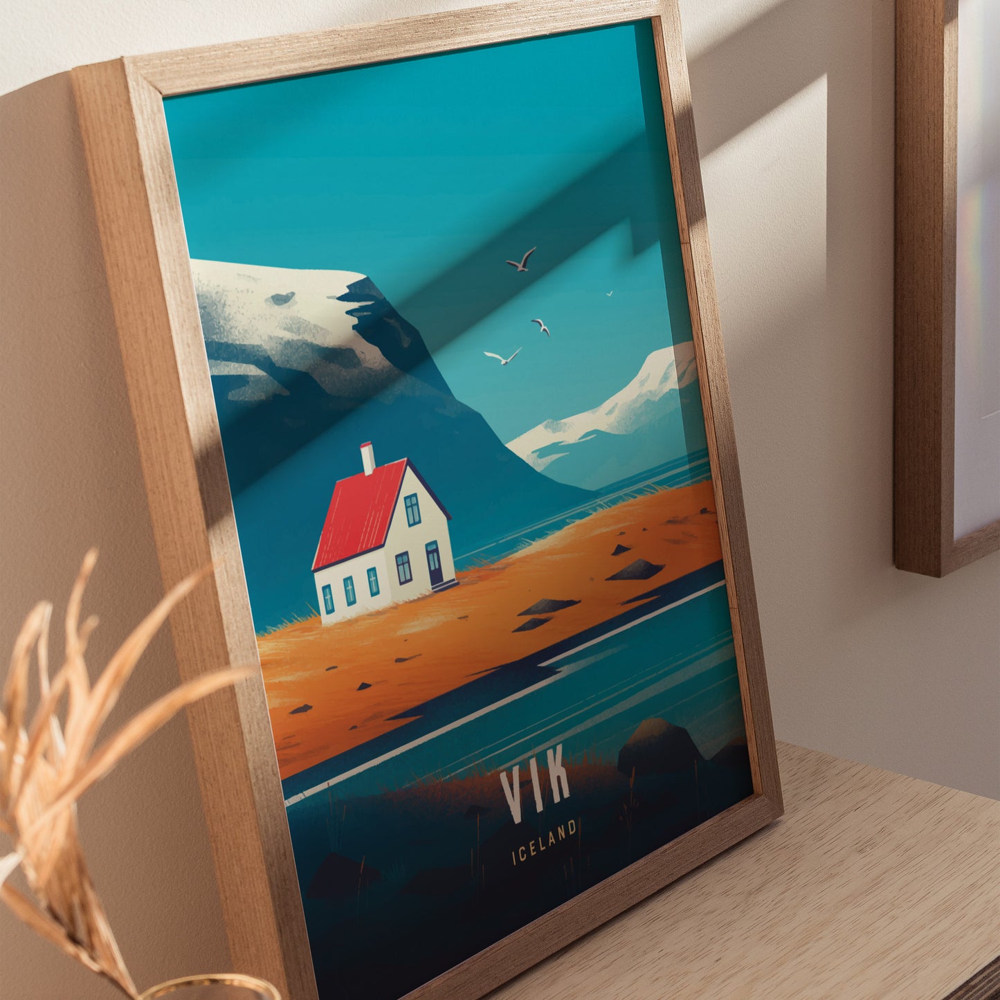 A framed poster depicting a minimalist landscape with a white house, red roof, mountains, and seagulls against a blue sky, labeled Vik Iceland.