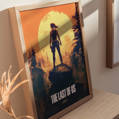 Framed poster of The Last of Us featuring Abby silhouetted against a large yellow sun in a forest setting, displayed on a wooden surface.