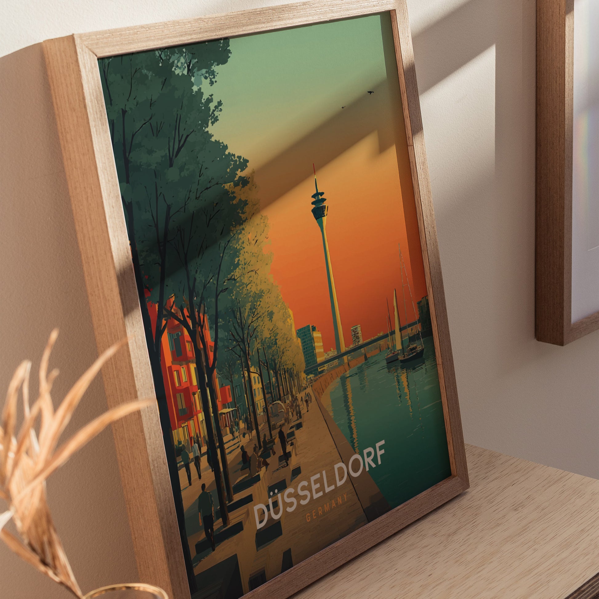 A framed poster of Düsseldorf, Germany, features a colorful illustration showcasing the citys skyline at sunset, with the iconic TV tower and a peaceful canal lined with trees and buildings.