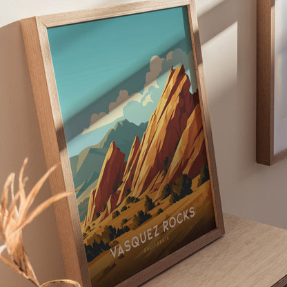 Framed poster of Vasquez Rocks, showcasing stylized orange sandstone formations under a blue sky with clouds. The artwork captures the iconic California landscape, resting on a wooden surface.