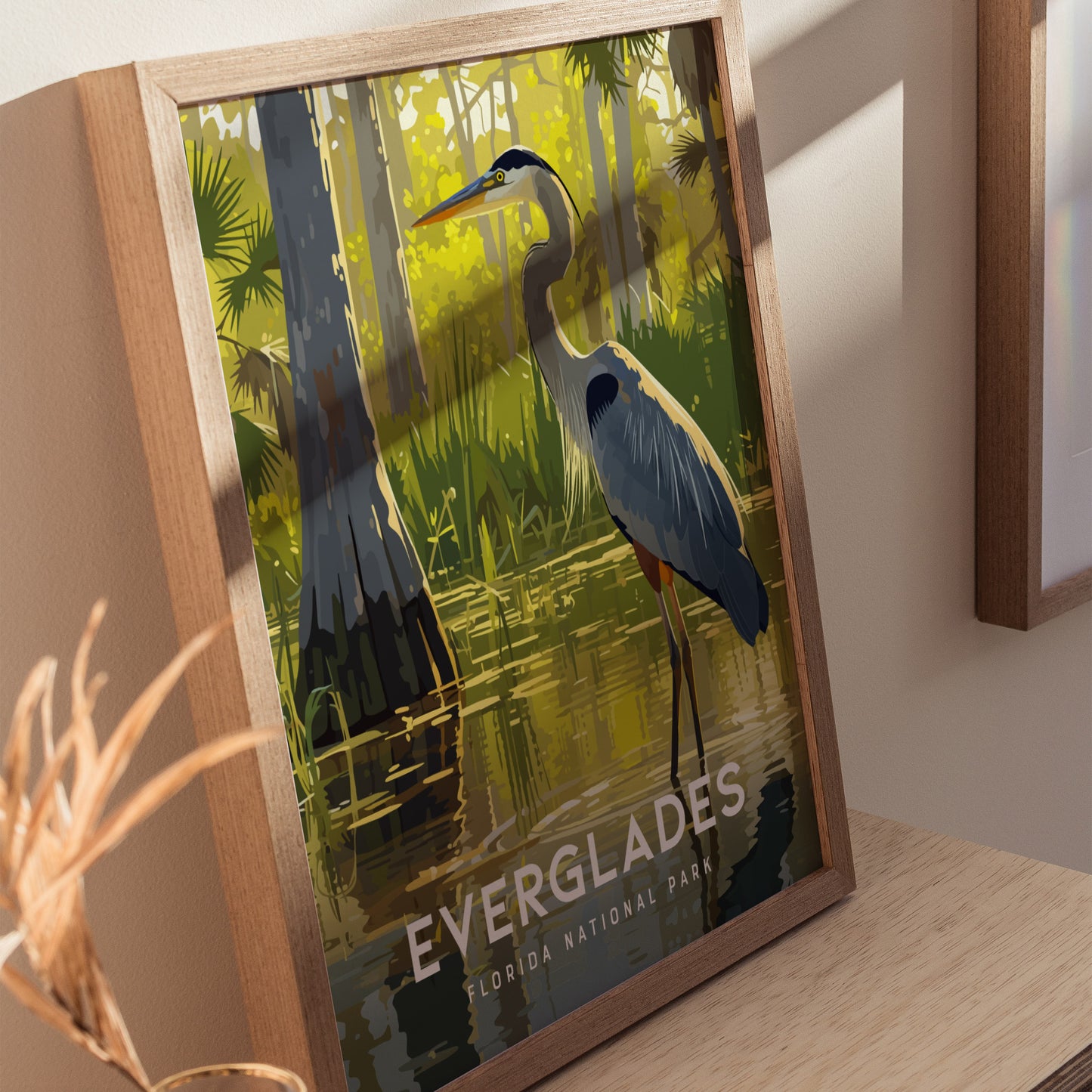 A framed art print of a Great Blue Heron wading in a sunlit, lush Everglades scene with cypress trees. The text reads Everglades Florida National Park.