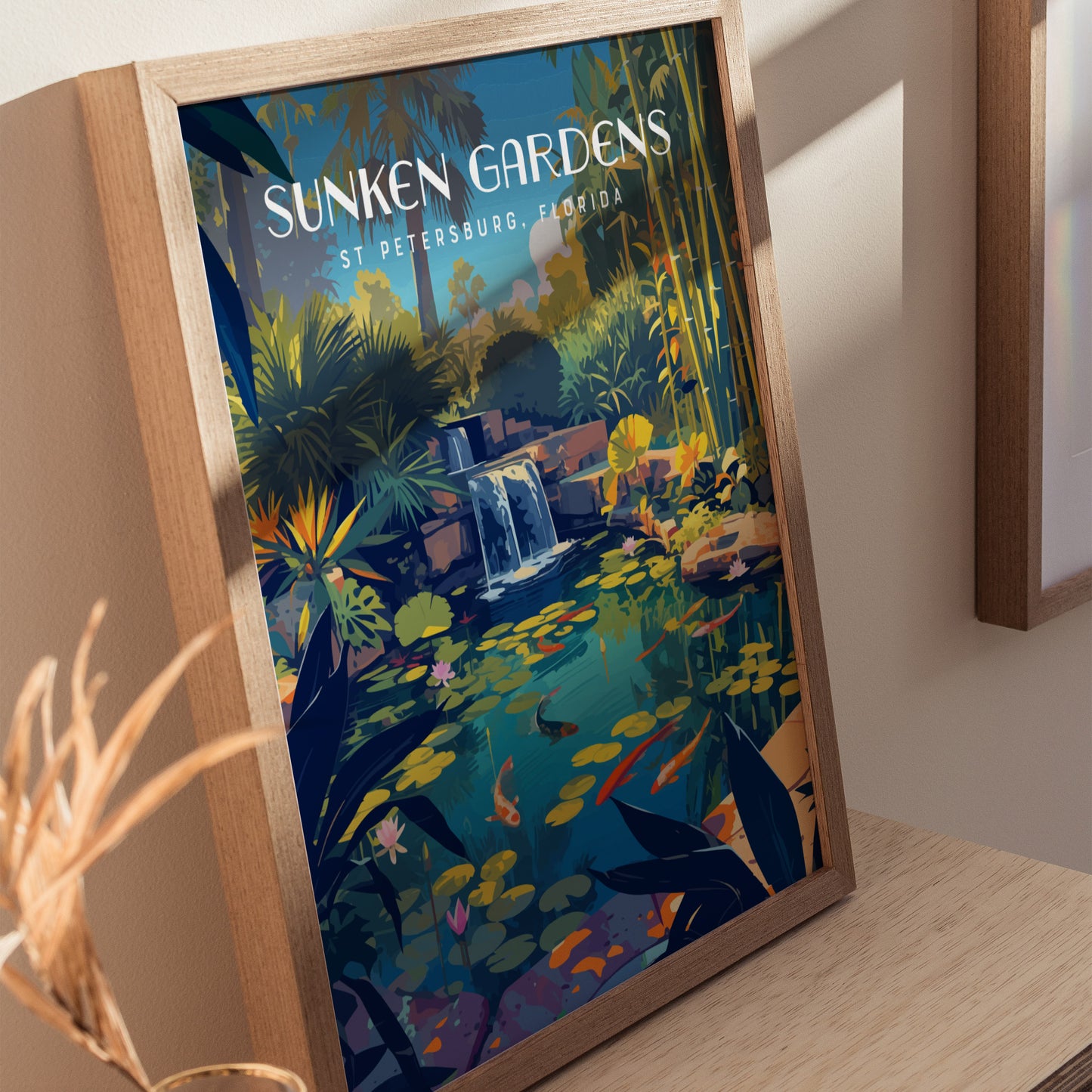 Framed poster featuring a tropical scene with a koi pond, lush foliage, and a waterfall, titled Sunken Gardens St Petersburg, Florida, resting on a wooden surface.