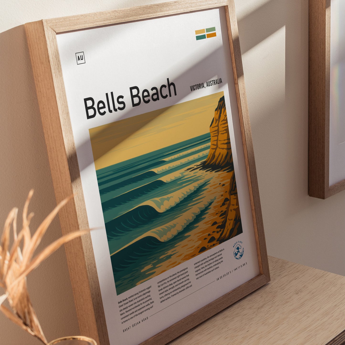 A framed poster of Bells Beach in Victoria, Australia, featuring stylized waves and cliffs in golden and teal hues, is displayed on a wooden surface with soft shadows.