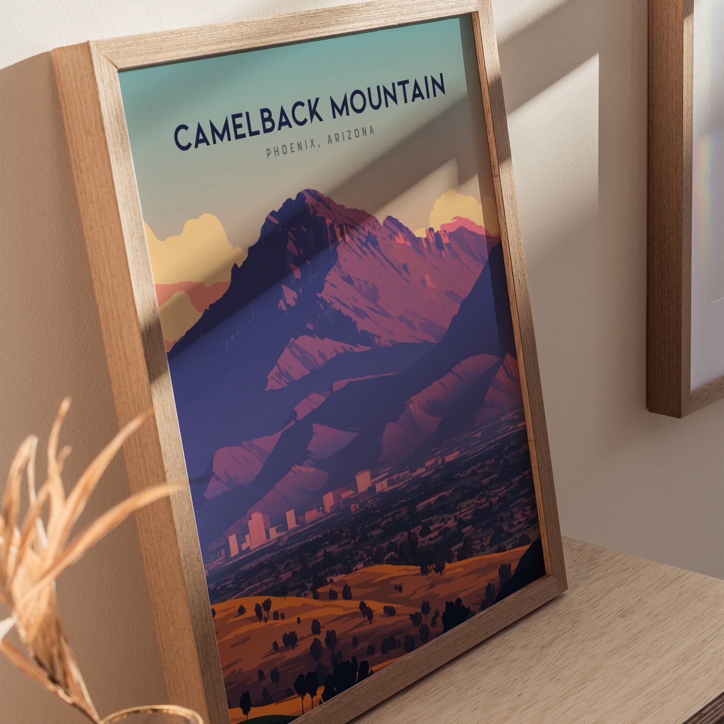 Framed poster of Camelback Mountain in Phoenix, Arizona, featuring vibrant desert colors and a dramatic silhouette. Positioned on a wooden surface, it captures the beauty of the Sonoran Desert.