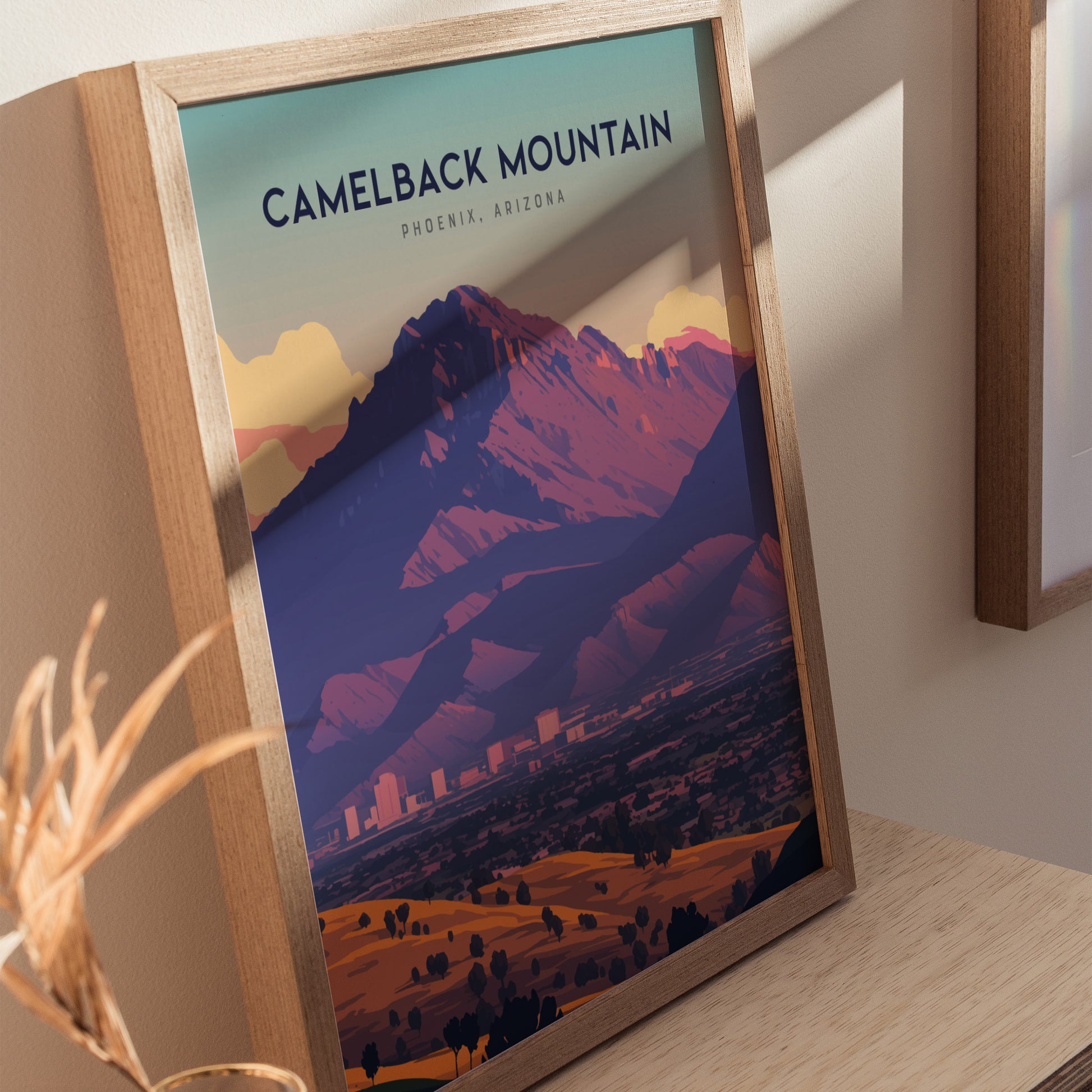 Framed poster of Camelback Mountain in Phoenix, Arizona, featuring vibrant desert colors and a dramatic silhouette. Positioned on a wooden surface, it captures the beauty of the Sonoran Desert.