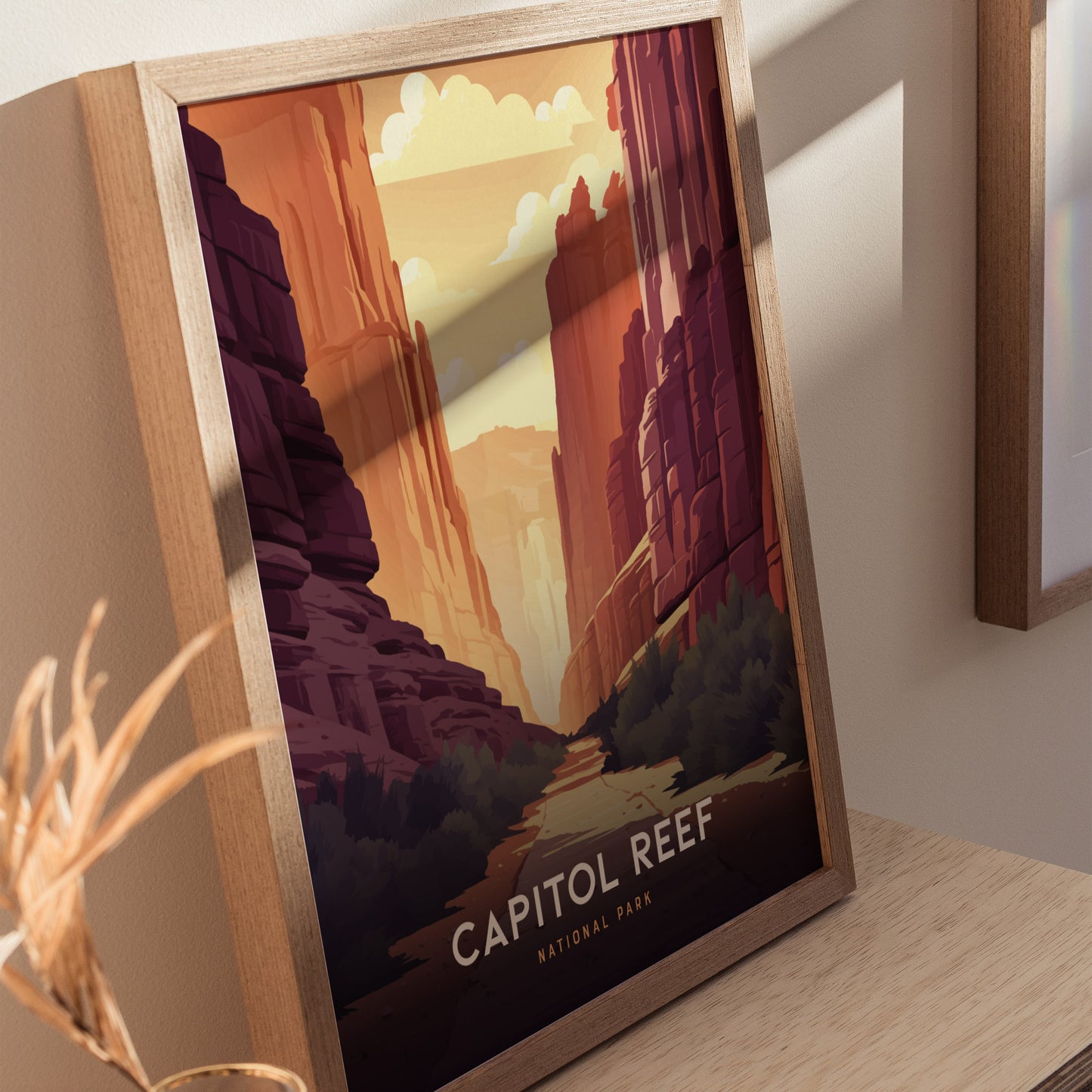 Framed art print of Capitol Reef National Park featuring vibrant red rock canyons and a sunlit sky, displayed on a wooden surface with nearby decorative elements.