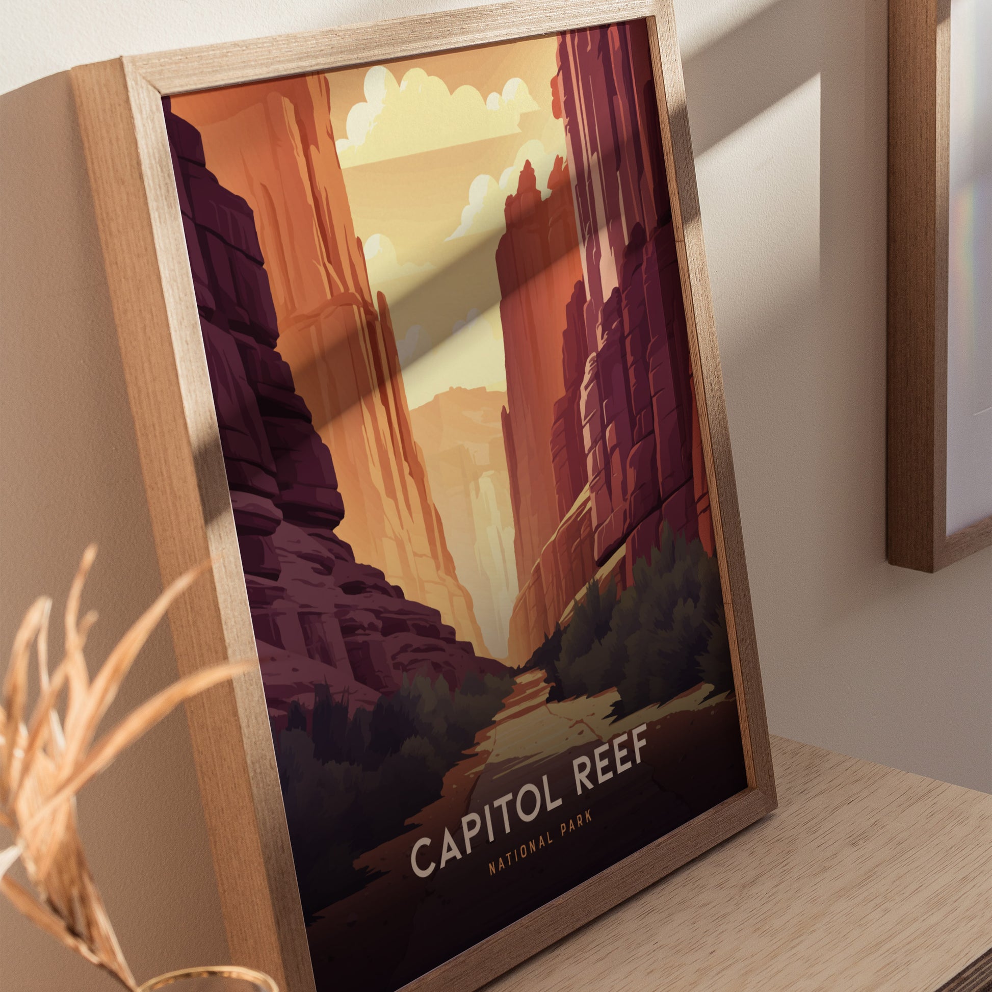 Framed art print of Capitol Reef National Park featuring vibrant red rock canyons and a sunlit sky, displayed on a wooden surface with nearby decorative elements.