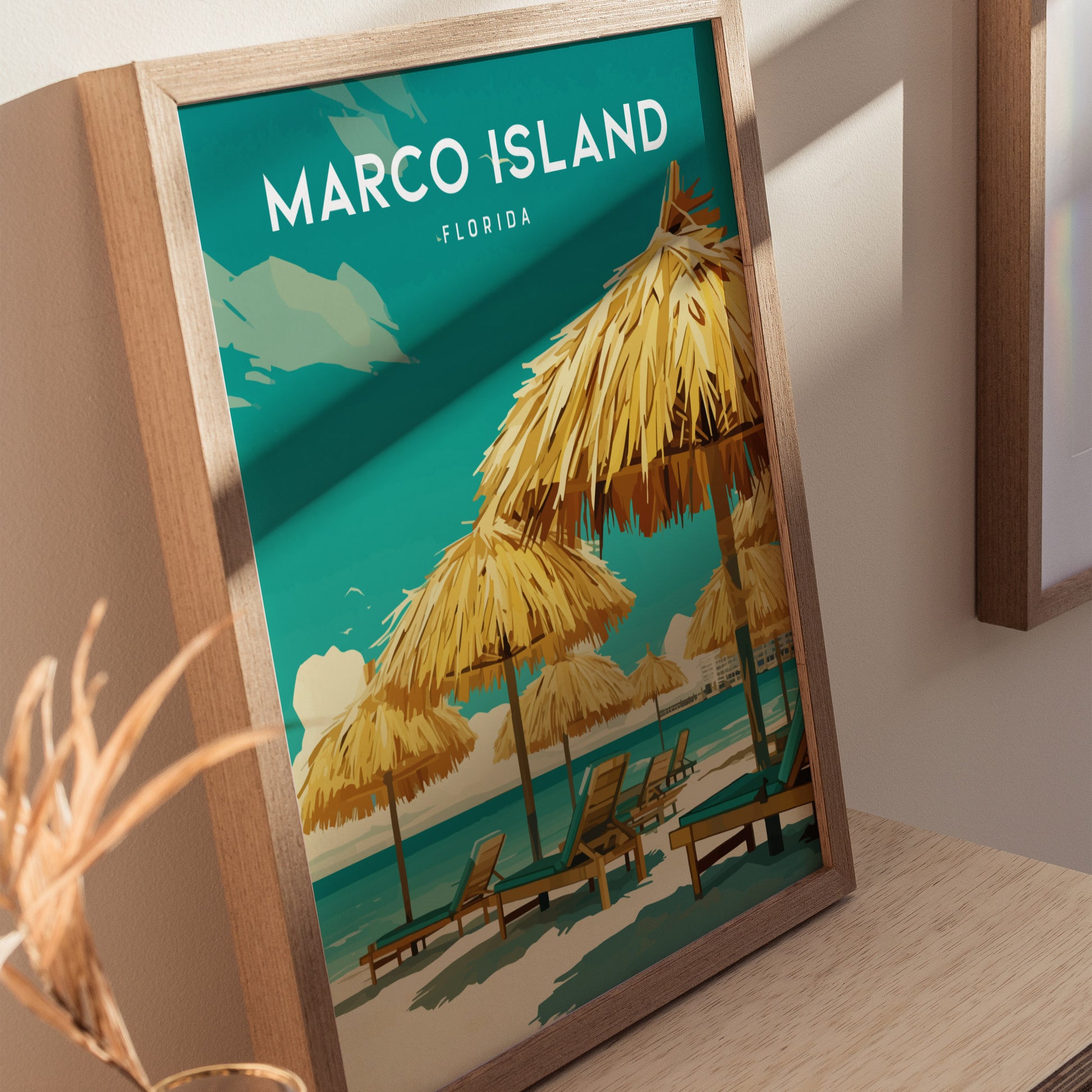 A framed poster featuring Marco Island Florida with illustrations of beach umbrellas and lounge chairs on a sandy shore against a turquoise sea, displayed on a wooden surface.