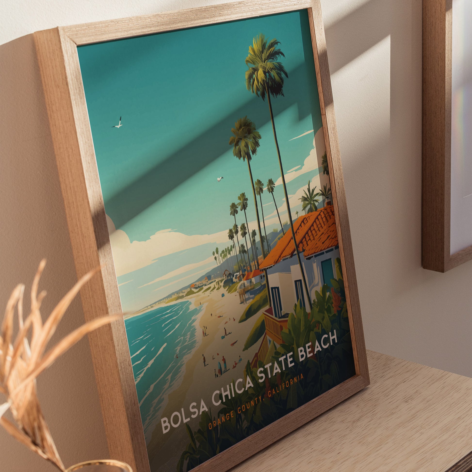 A framed poster of Bolsa Chica State Beach shows a scenic view with palm trees, beachgoers, and ocean waves. The artwork features vibrant colors and a sunny atmosphere.