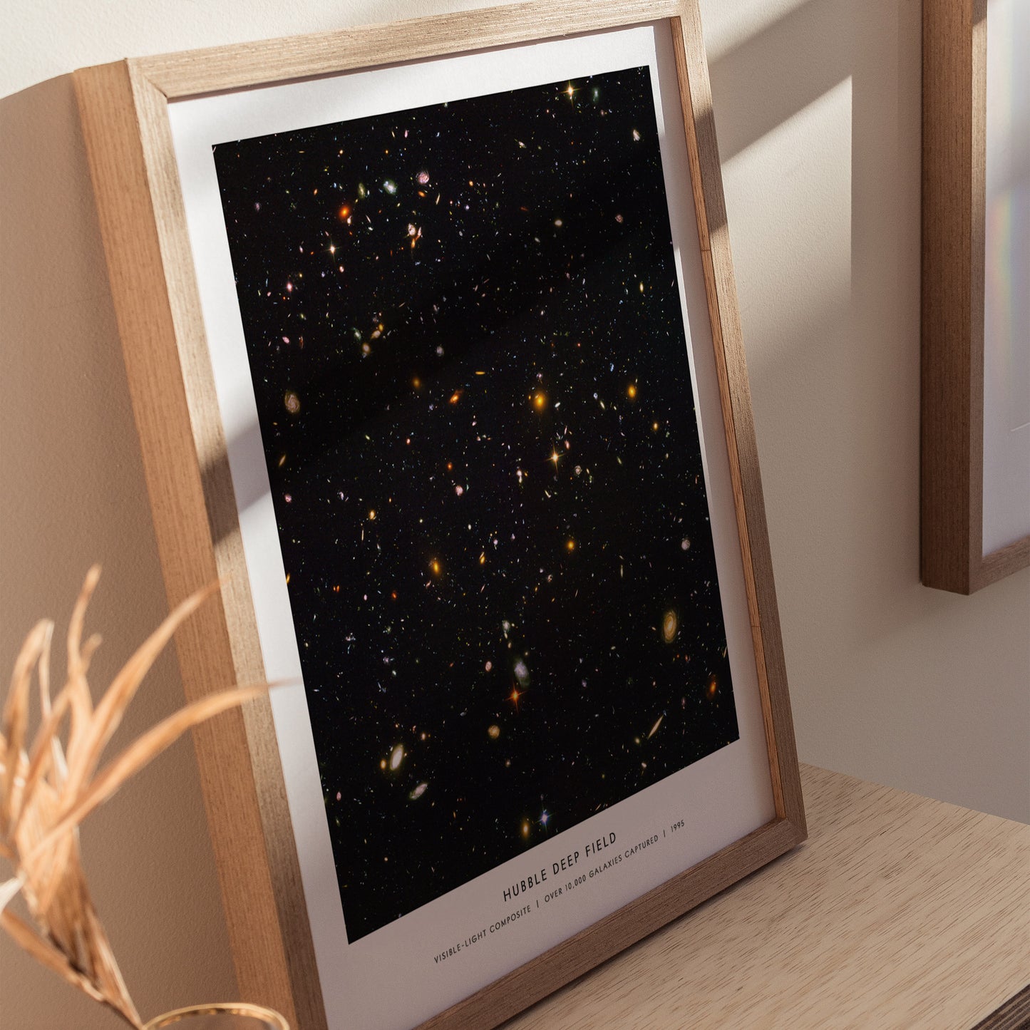 Natural wood framed Hubble Deep Field space print leaning on a shelf next to plants and neutral accessories
