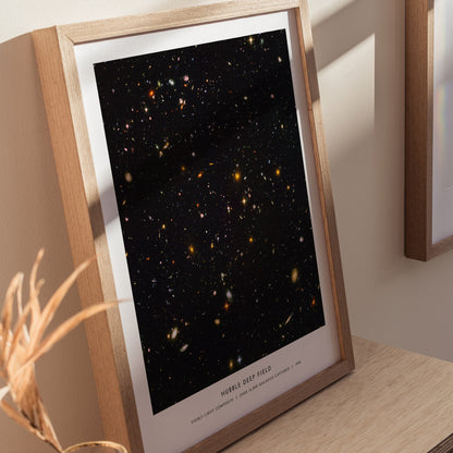 Natural wood framed Hubble Deep Field space print leaning on a shelf next to plants and neutral accessories