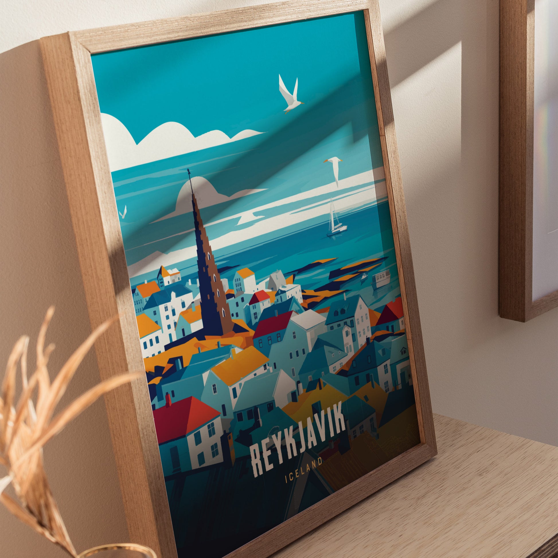 Framed Reykjavík travel poster featuring colorful buildings, a prominent church spire, and seagulls flying over a coastal landscape. The artwork is displayed on a light wood surface.
