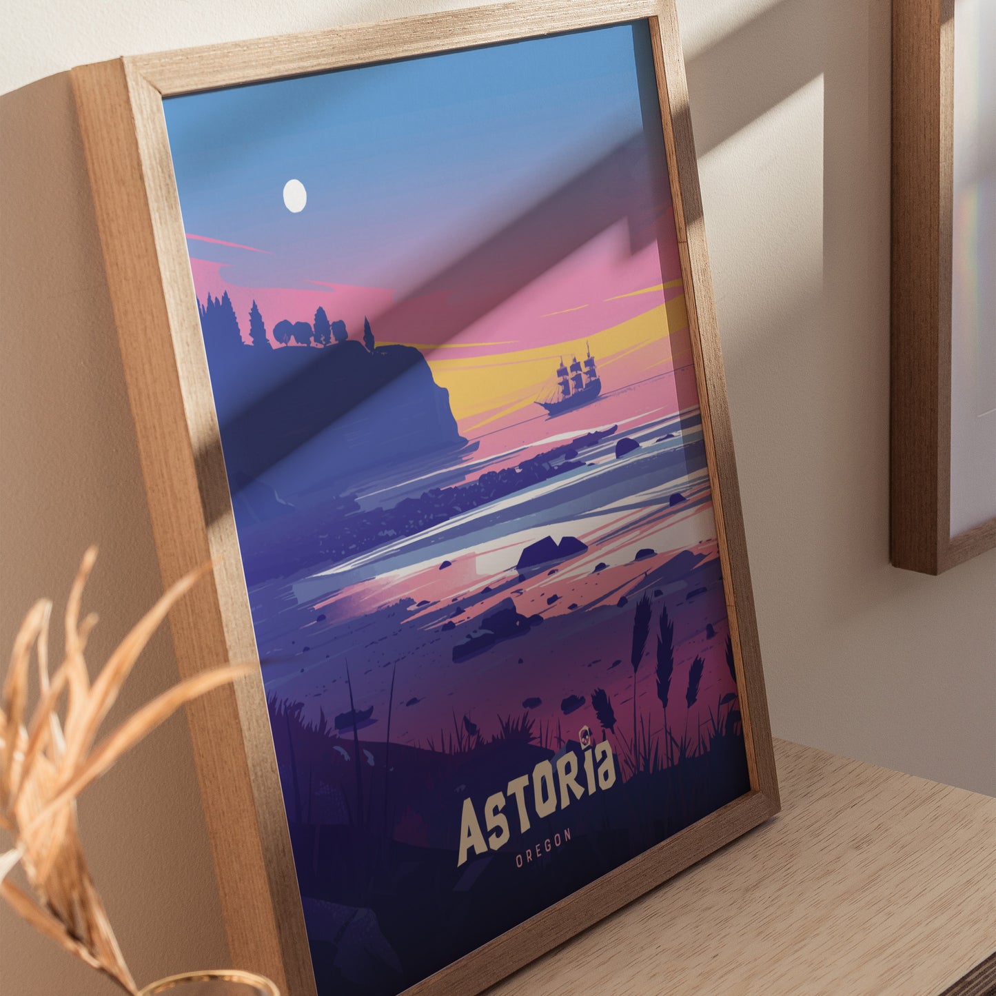A framed poster of Astoria, Oregon, features a colorful illustration of a pirate ship sailing near a rugged coastline at sunset, with the word Astoria prominently displayed.