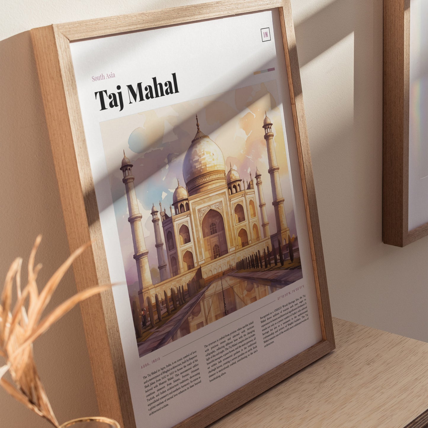 Framed watercolor illustration of the Taj Mahal with a detailed description below, set against a warm, softly lit background. A decorative plant is partially visible in the foreground.