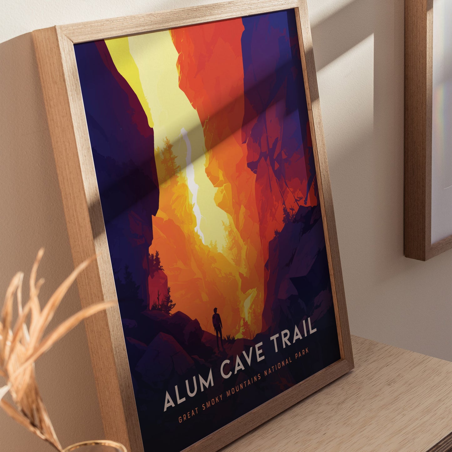 A framed poster depicting a hiker silhouetted against a vibrant, abstract landscape of orange and yellow cliffs, titled Alum Cave Trail, Great Smoky Mountains National Park.
