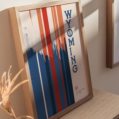 A framed poster with vertical red, blue, and white stripes, featuring the word WYOMING in bold blue letters. It rests on a wooden surface.