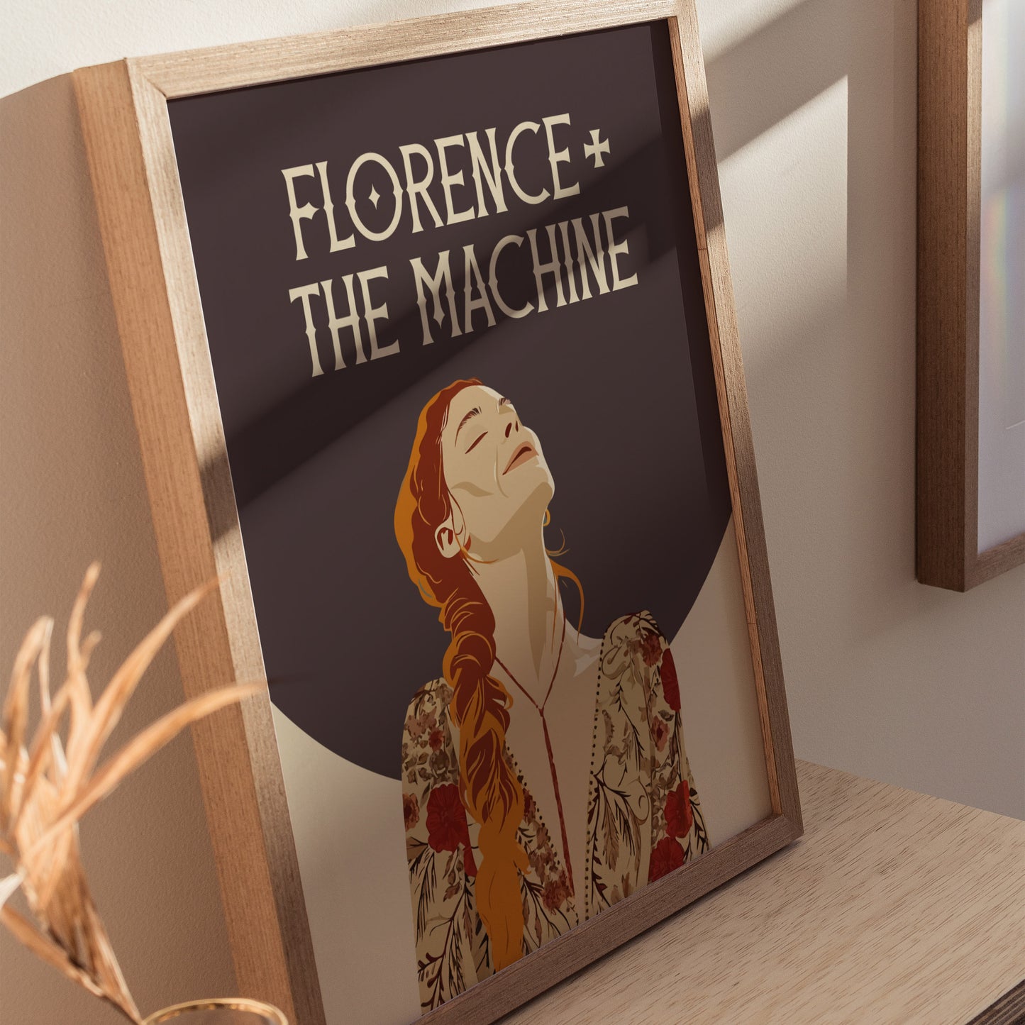 A framed poster of Florence + The Machine featuring an illustrated woman with red hair in a floral dress, set against a dark background. Sunlight casts shadows on the surface.