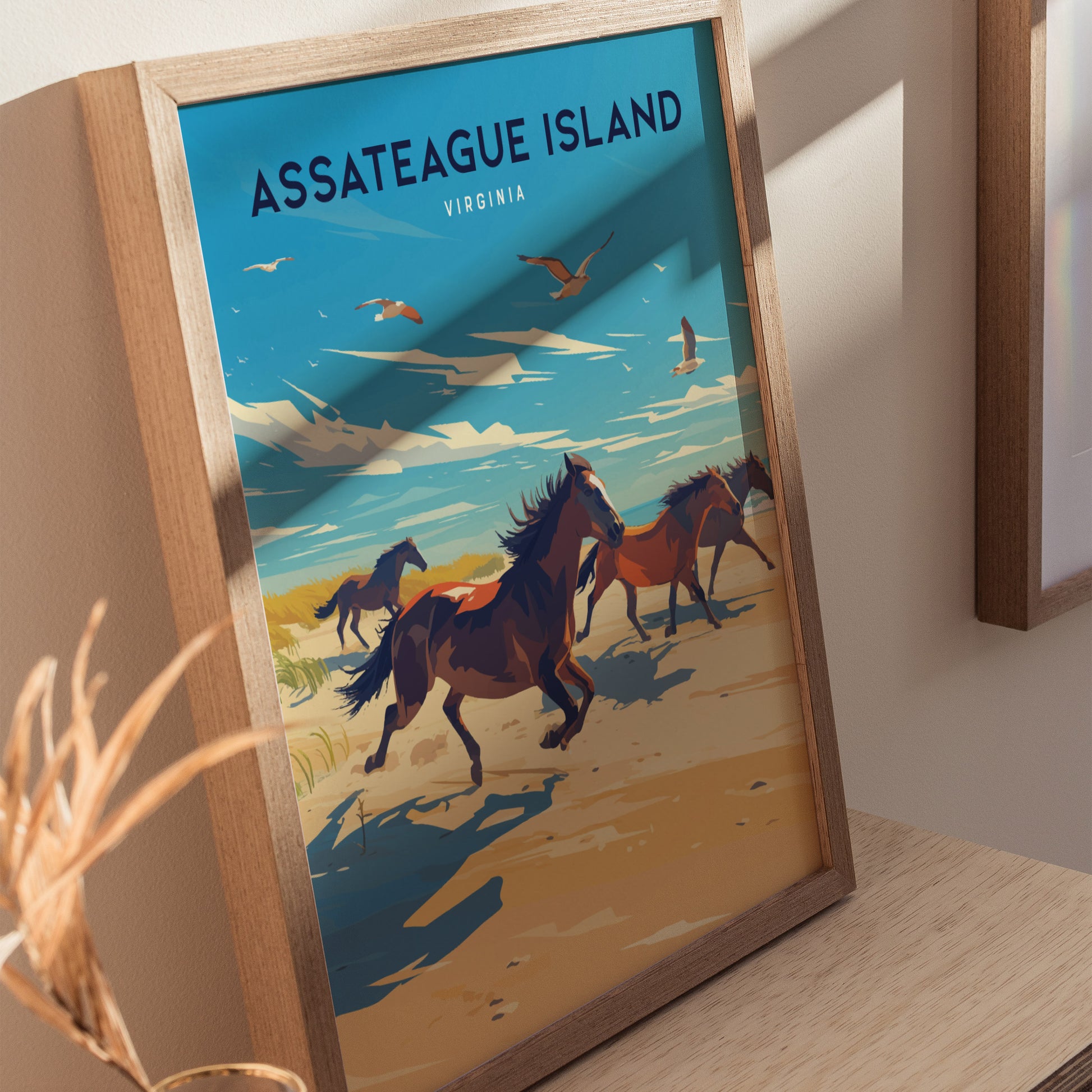 Framed Assateague Island poster depicting wild horses running along a sandy beach under a blue sky with seagulls. The artwork is set against a light-colored wall.