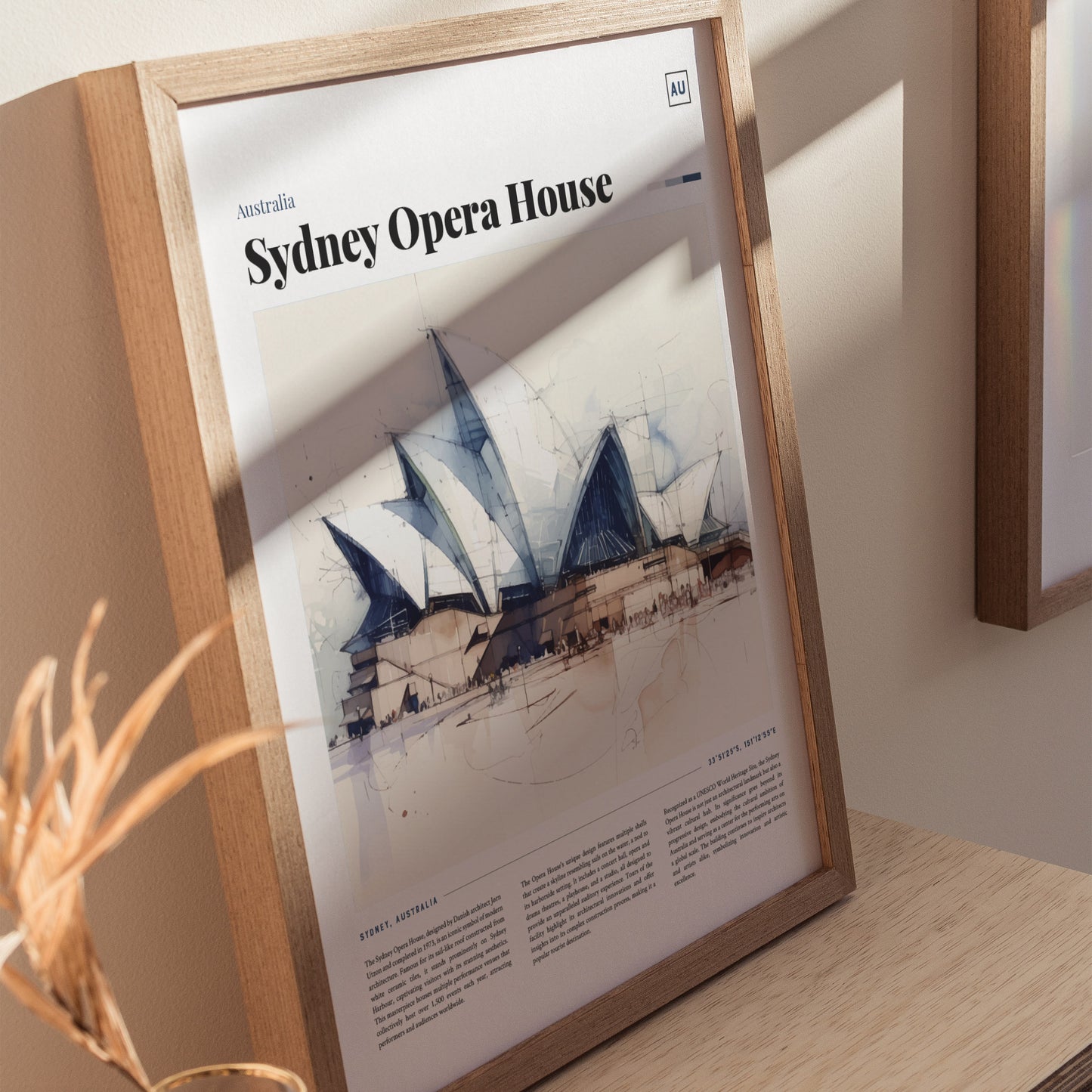 Framed Sydney Opera House poster featuring a watercolor illustration with sail-shaped shells. It is displayed on a light wooden surface with a shadow cast across the image.