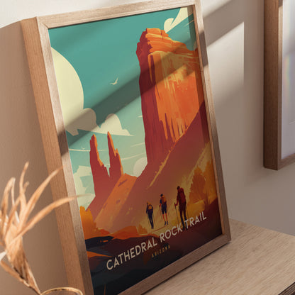 Framed poster depicting Cathedral Rock Trail in Sedona, Arizona, featuring vibrant red cliffs and hikers under a blue sky with clouds. The artwork rests on a wooden surface.