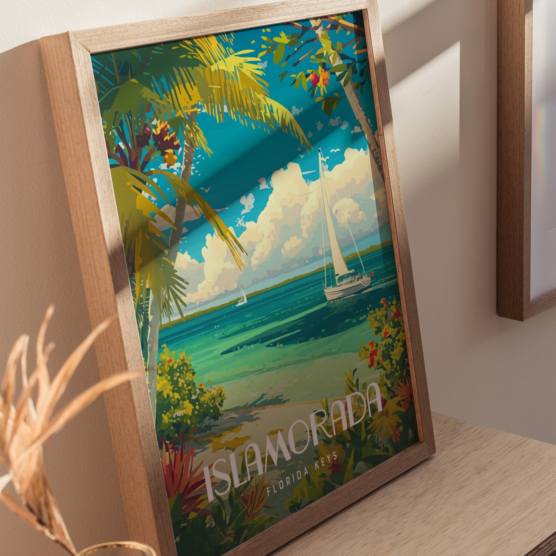 A colorful poster of Islamorada, Florida Keys, features palm trees, turquoise waters, a sailboat, and vibrant foliage, all framed in wood and leaning against a light-colored wall.
