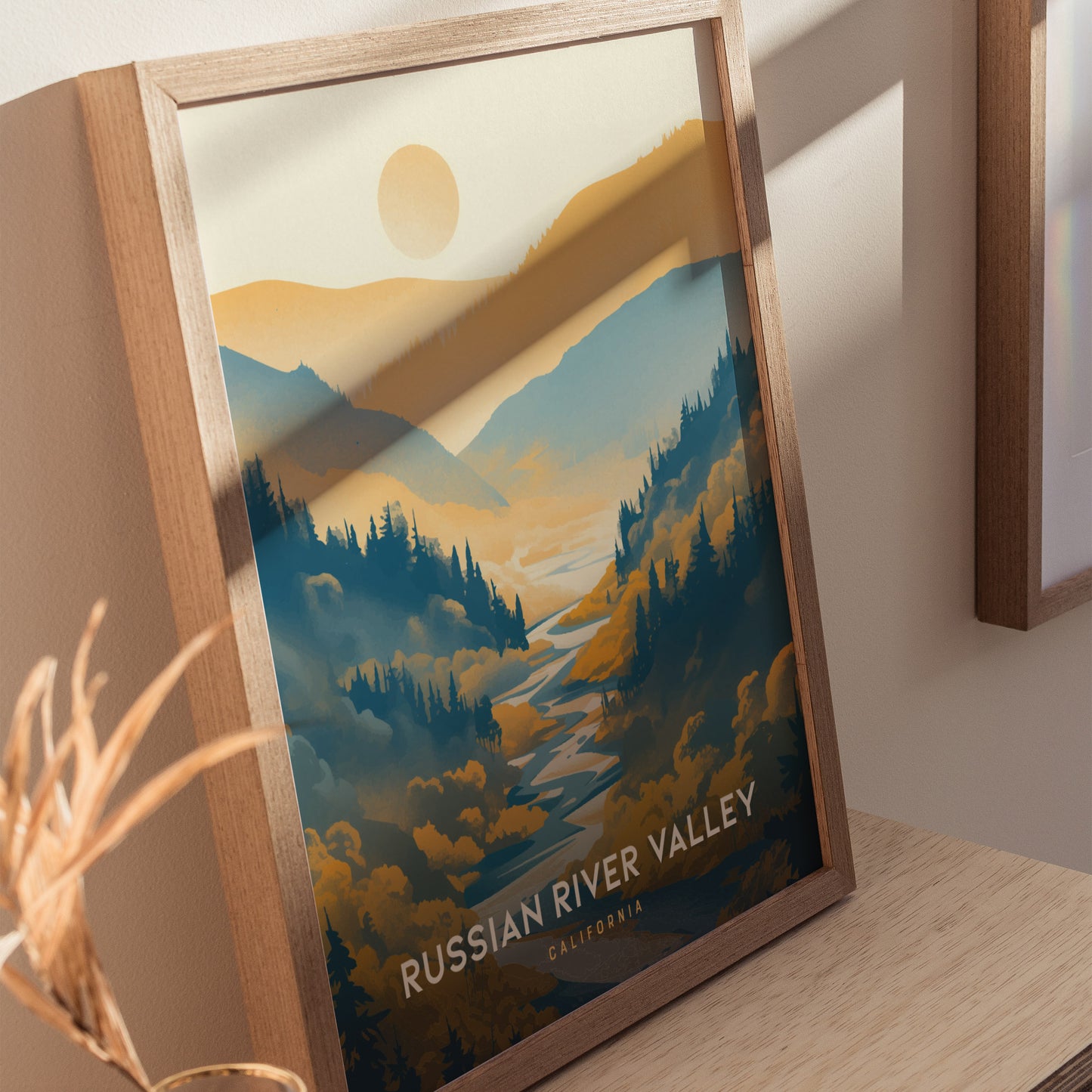 Framed poster of Russian River Valley, featuring stylized blue and golden rolling hills with a sun in the background, displayed on a wooden surface.