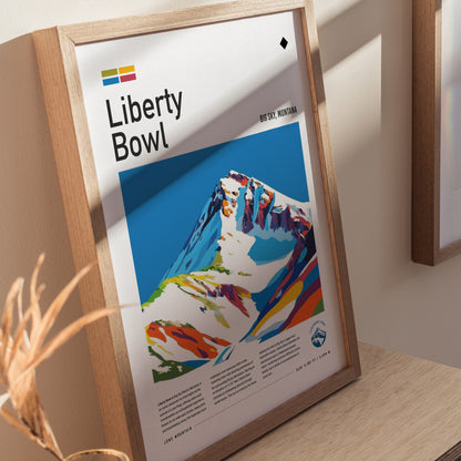 Framed poster of Liberty Bowl at Big Sky, Montana, featuring a colorful, stylized mountain illustration. The artwork is displayed on a wooden surface with soft natural lighting.