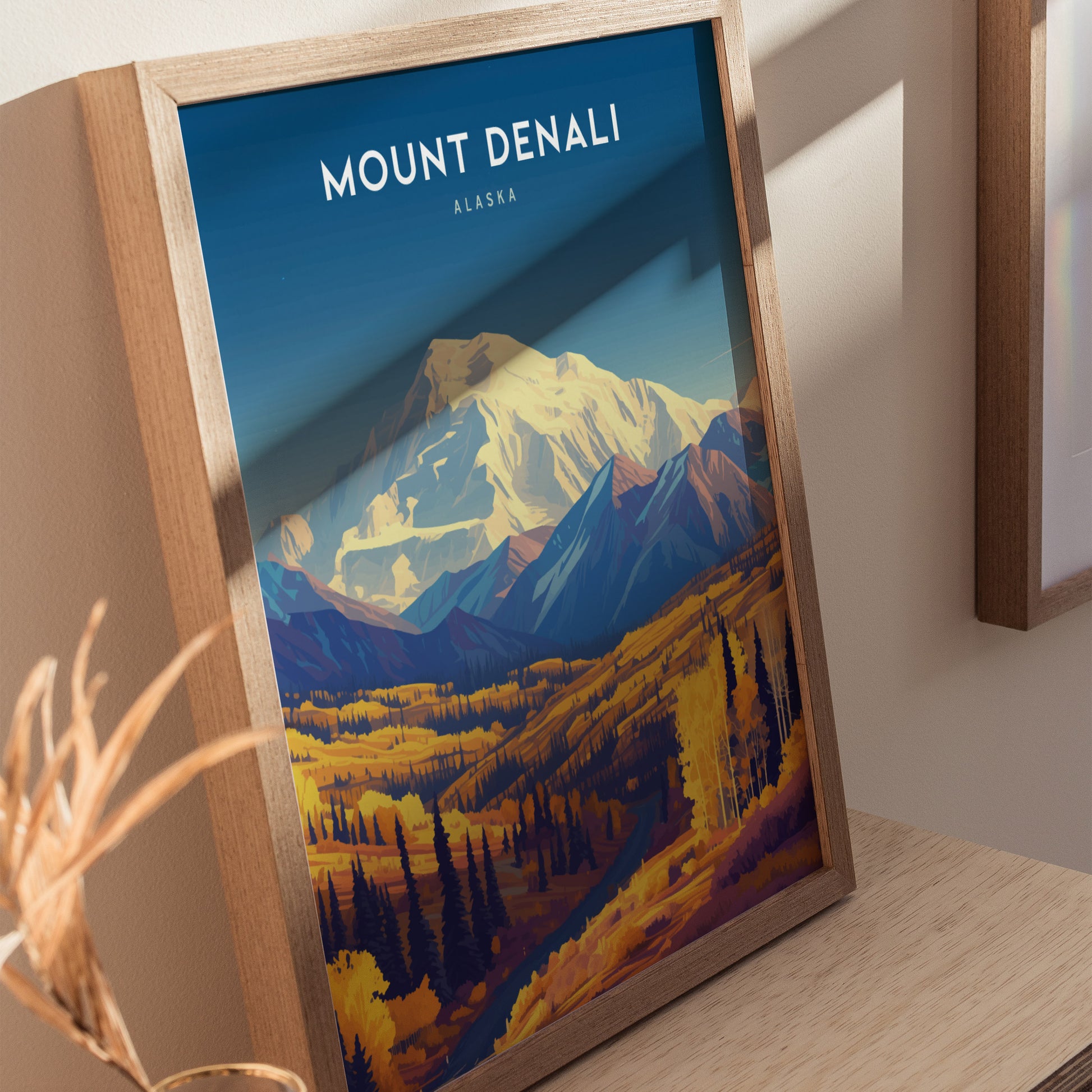 Framed poster of Mount Denali with vibrant autumnal colors, showcasing the mountain and surrounding landscape under a clear blue sky. The artwork is set on a wooden table.