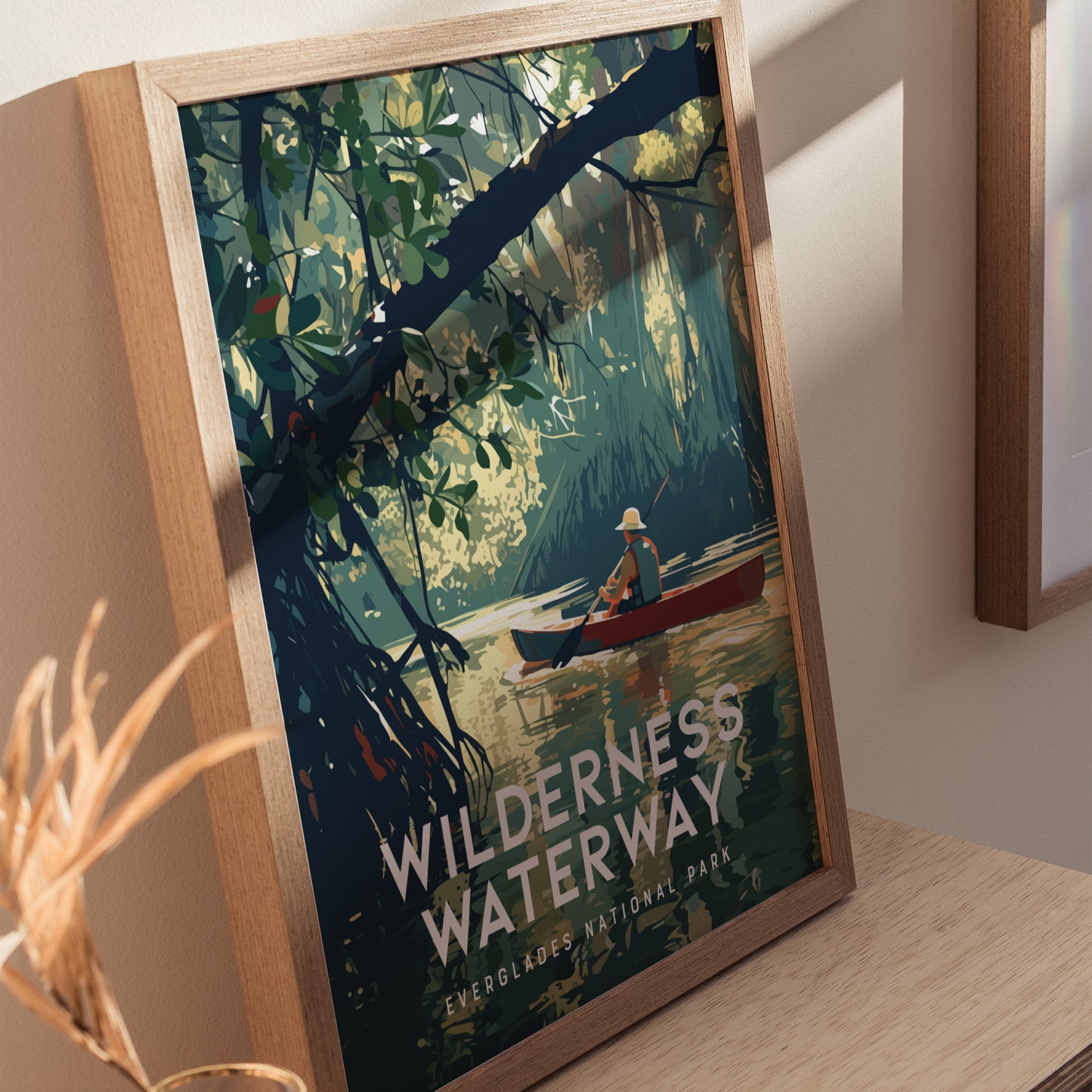 A framed poster titled Wilderness Waterway depicts a lone canoer paddling through a lush, green mangrove forest in Everglades National Park. Sunlight filters through the dense foliage.