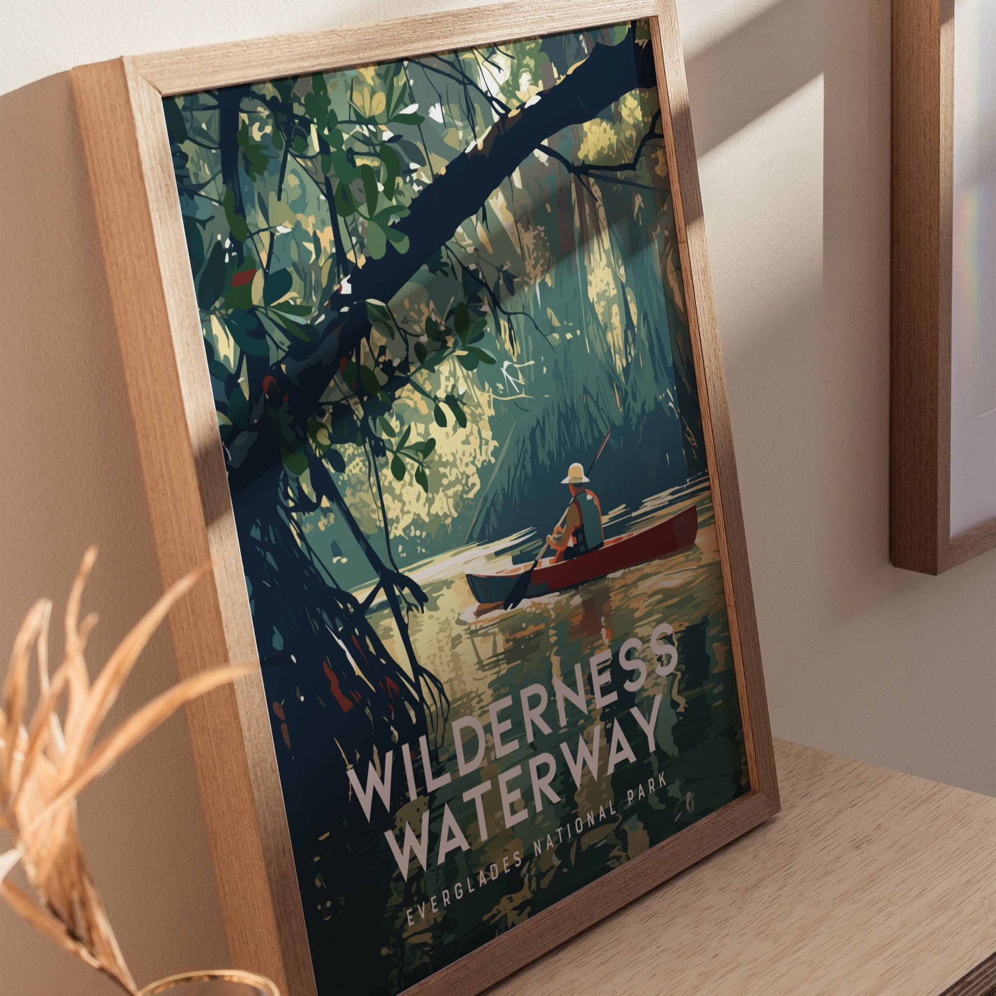 A framed poster titled Wilderness Waterway depicts a lone canoer paddling through a lush, green mangrove forest in Everglades National Park. Sunlight filters through the dense foliage.
