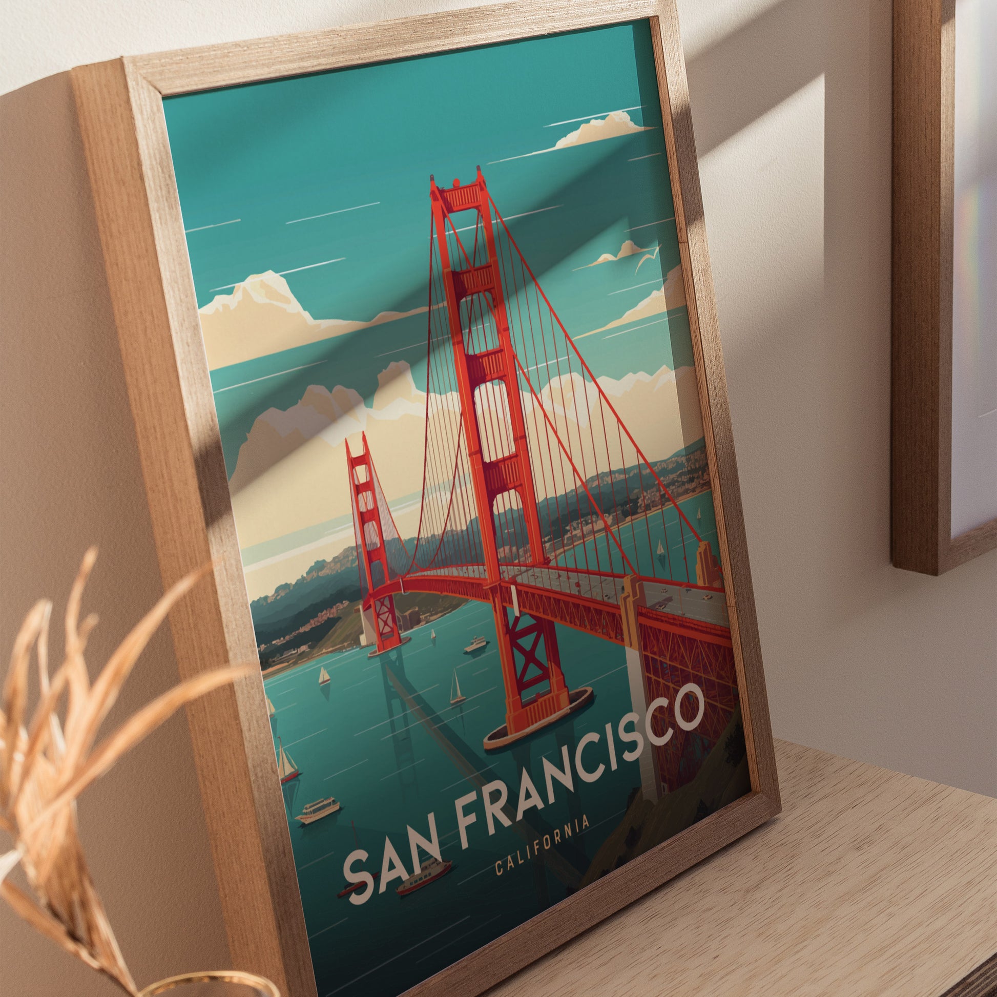 Framed poster of the Golden Gate Bridge in vibrant red under a clear blue sky, with sailboats in the bay, titled San Francisco, California, leaning against a wall.