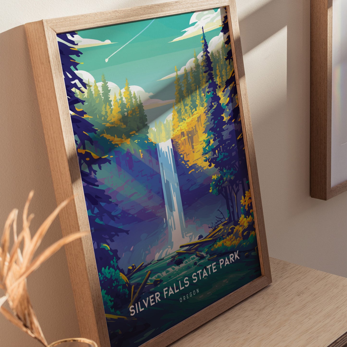 A framed poster of Silver Falls State Park, featuring a stylized waterfall surrounded by vibrant trees under a bright sky, leaning against a light-colored wall.